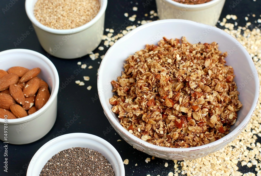 Homemade granola in white bowl with almond and seeds on black background Homemade granola in white bowl with almond and seeds on black background