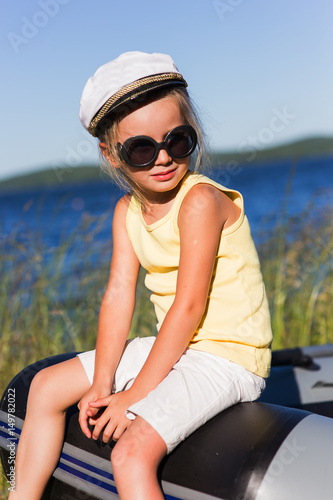 Girl in sailor cap on the lake in summer sunny day on vacation.
