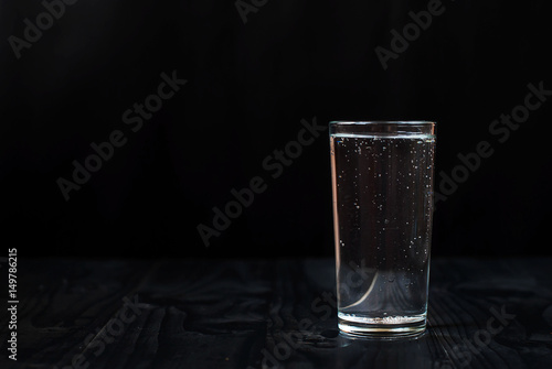 Just a glass of water on a black background. Mineral water in a glass on a dark wooden table.