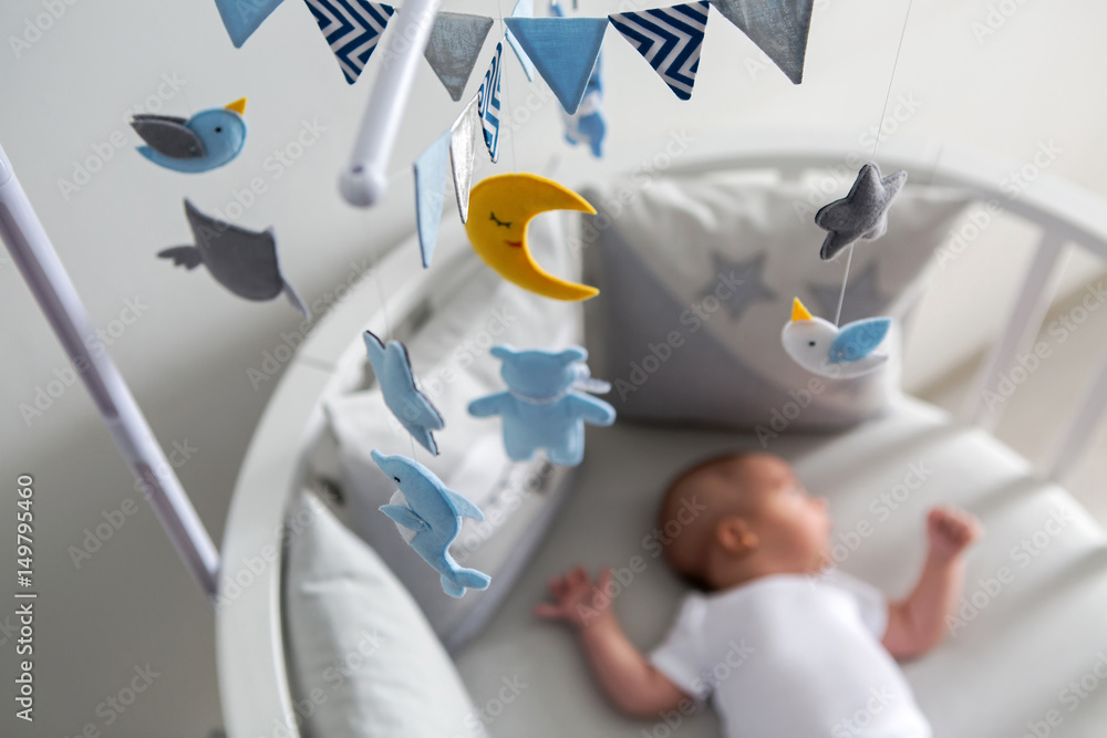 newborn lies in the round white bed with mobile and toys