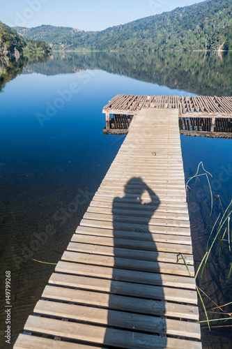 Wooden pier and photographer's silhouette at Lago Tilquilco lake in National Park Huerquehue, Chile photo