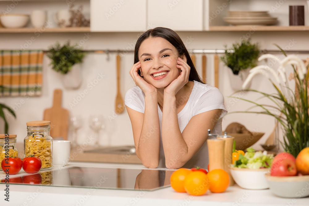 Young woman standing near desk and laptop in the kitchen, smiling Young woman standing near desk and laptop in the kitchen, smiling