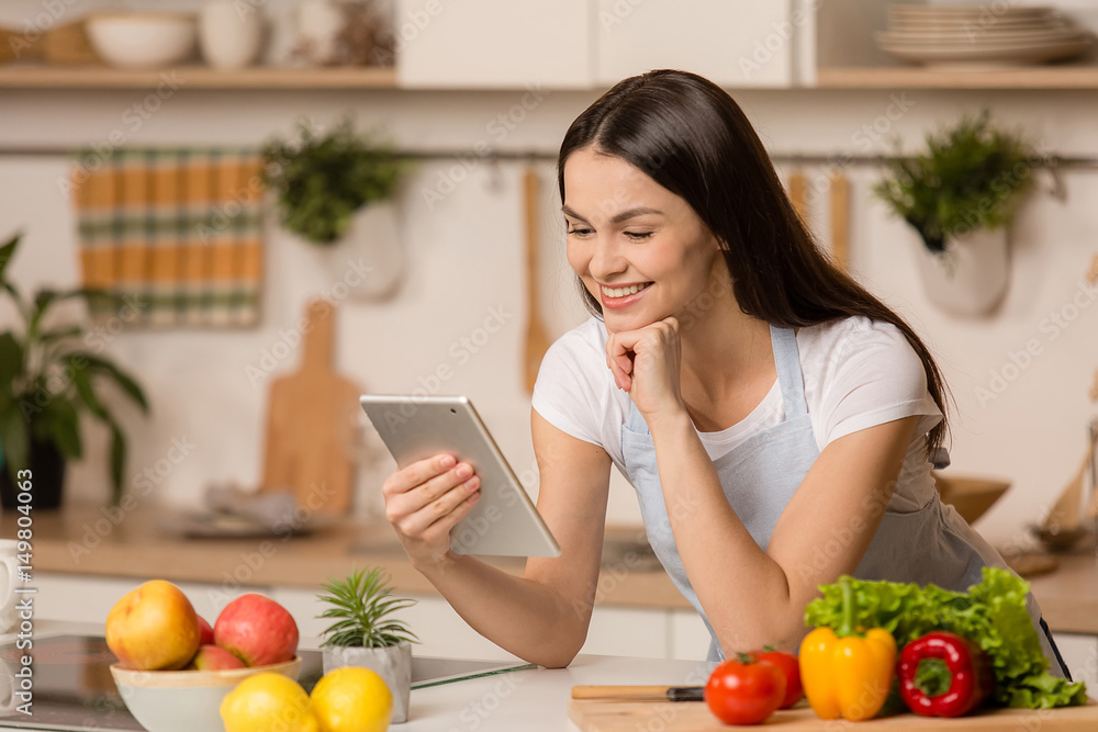 Young Woman standing in kitchen with tablet computer and looking recipes.