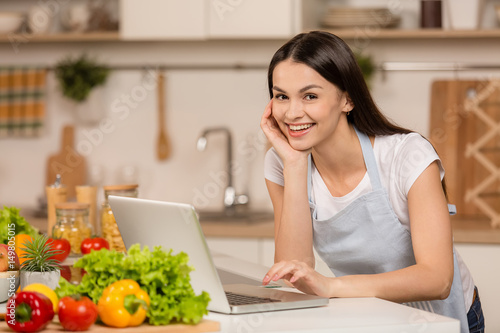 Young Woman in kitchen with laptop computer looking recipes  smiling. Food blogger concept