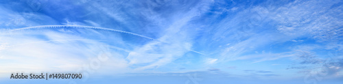 Panorama of a blue sky with clouds and an inverse trail from a jet plane