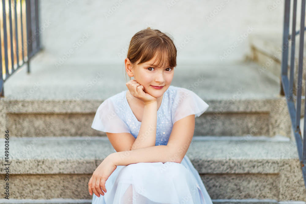 Sweet little preteen girl wearing party dress, sitting on stairs