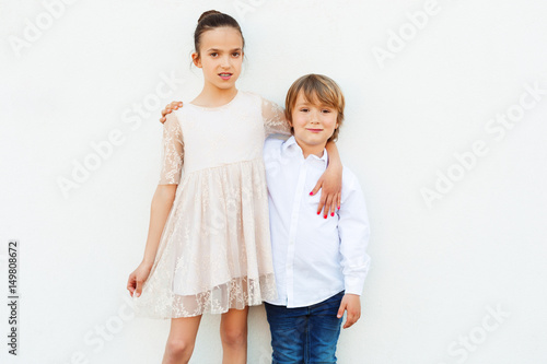 Group of two kids, girl and boy, wearing party clothes, standing against white background