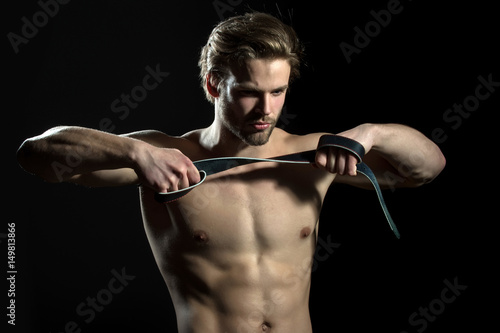 Belt is in the hands of naked man. The guy does exercises for hands with leather belt. Sexy model for men's accessories. Concentration and meditation in the gym © Tverdokhlib
