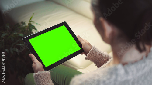 Indoor shot of a woman using tablet pc with green screen sitting on white sofa, horizontal orientation