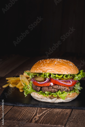 Fresh burger in bun with sesame with lettuce  tomato  beef and onion on wooden table.