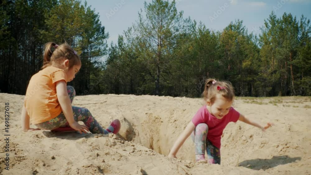 Two lovely girls play on the sand in the woods in the summer Two lovely girls play on the sand in the woods in the summer