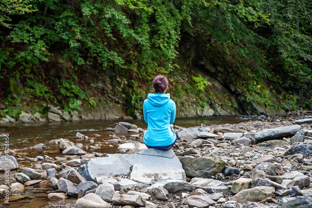The girl sits on a stone middle of the river. The concept of travel, leisure meditation.