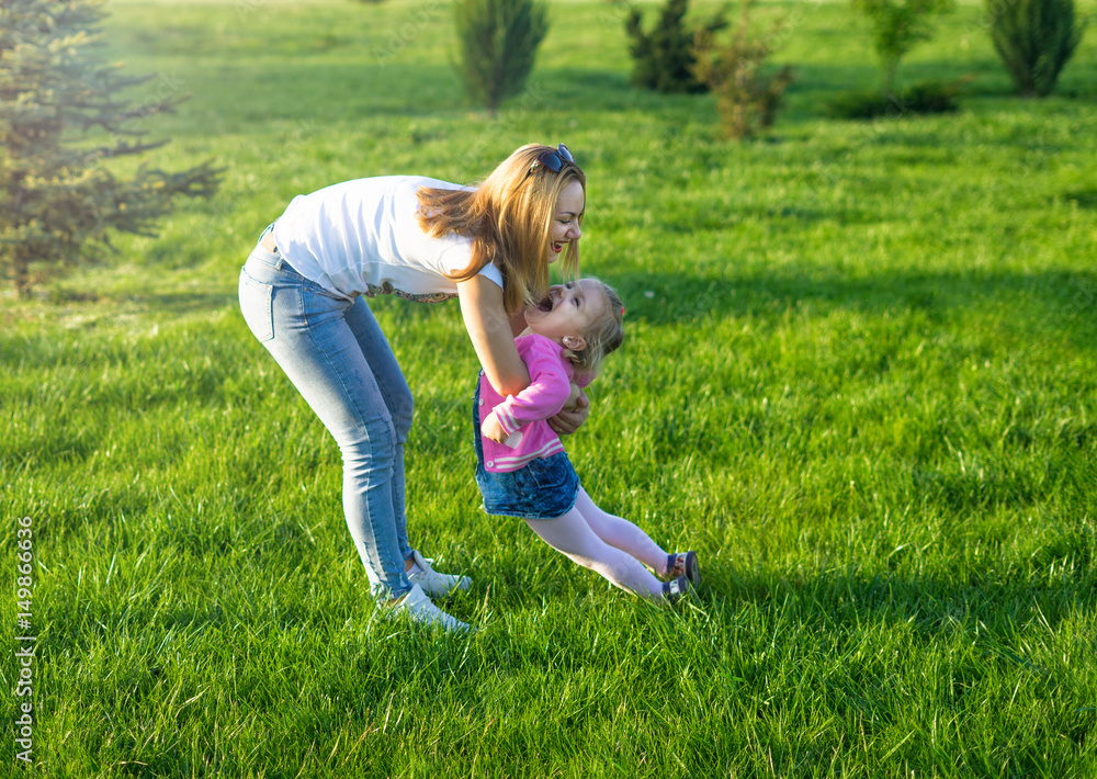 Beautiful mother playing with her cheerful girl. They are smiling. Happy family time playing with daughter in park. Beautiful mother playing with her cheerful girl. They are smiling. Happy family time playing with daughter in park.