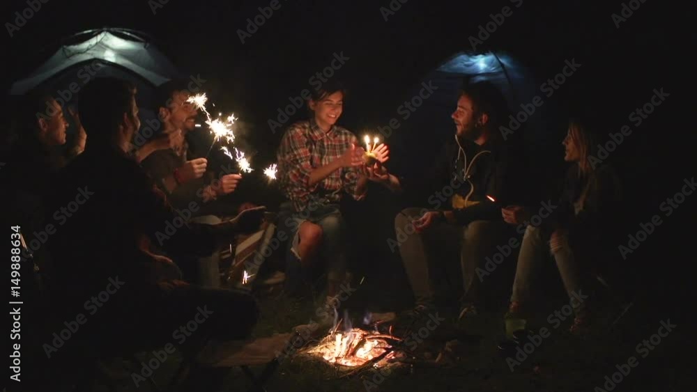 Group of friends with sparklers having fun around campfire and celebrate birthday Group of friends with sparklers having fun around campfire and celebrate birthday