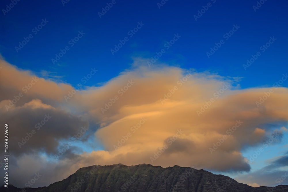 A hike of mountain with orange sunset clouds above on blue sky background