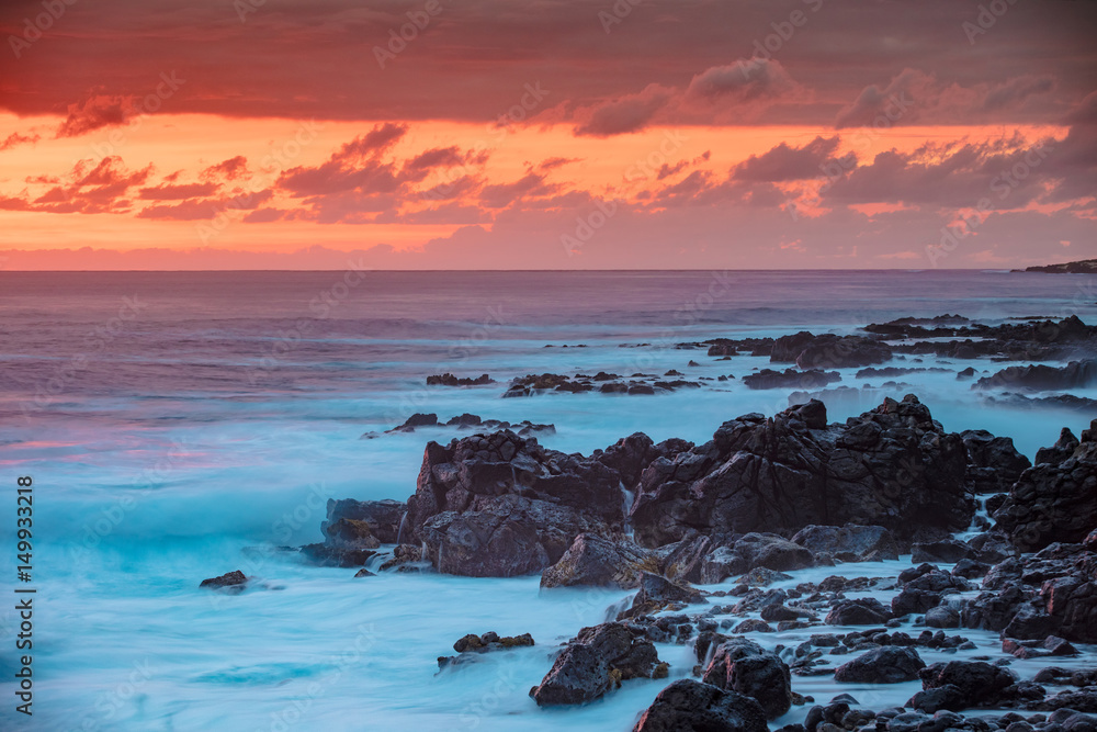 Beautiful red orange sunset in Pacific ocean. White splashes of ocean waves breaking against rocky coast.