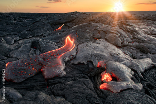 Black lava field with hot red orange Lavaflow at sunset background