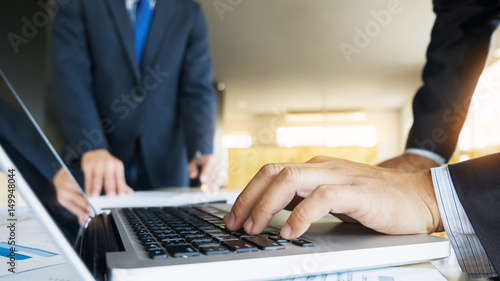 Closeup of businessman is keyboarding on portable net-book, while is sitting in modern office interior. Closely of a successful male entrepreneur is using laptop computer during work day in company