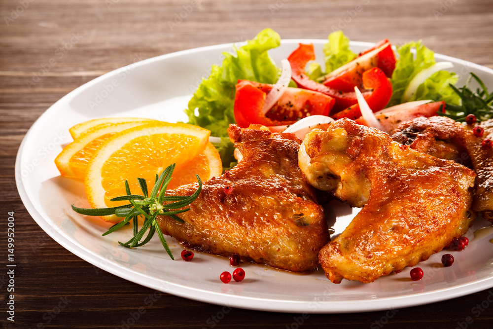 Roasted chicken wings with vegetable salad on wooden table Roasted chicken wings with vegetable salad on wooden table