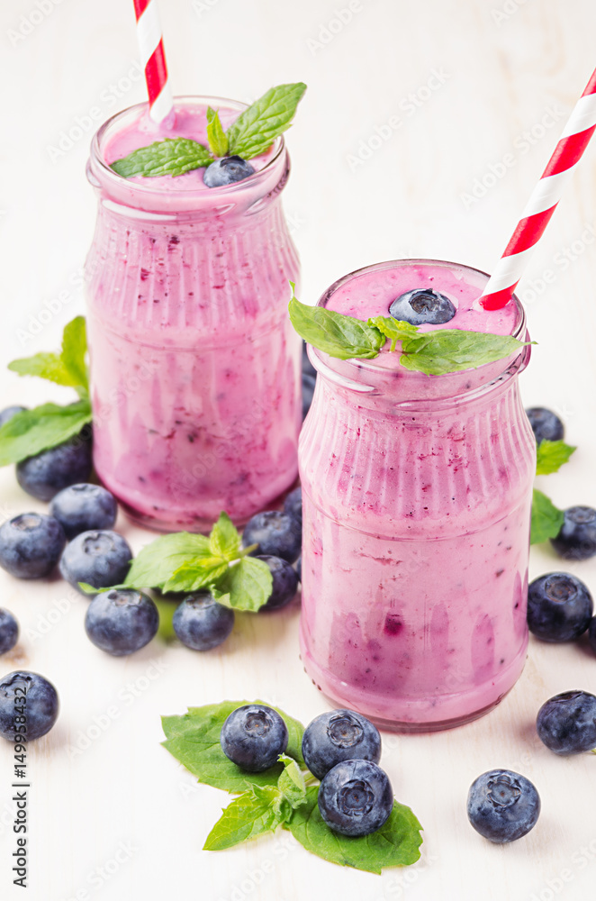 Violet blueberry fruit smoothie in glass jars with straw, mint leaves, berries. White wooden board background. Violet blueberry fruit smoothie in glass jars with straw, mint leaves, berries. White wooden board background.
