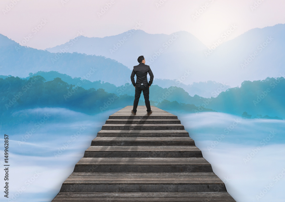 Businessman climbed on top of the stairs over the cityscape which can see beautiful scenary of mist with mountain range, Success business and Ambitions concept Businessman climbed on top of the stairs over the cityscape which can see beautiful scenary of mist with mountain range, Success business and Ambitions concept