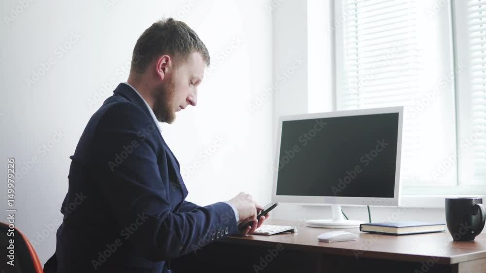 Businessman using his smartphone and surfing through the internet, sitting by the desk in his offiice. PC is turned off. Shot in 4k Businessman using his smartphone and surfing through the internet, sitting by the desk in his offiice. PC is turned off. Shot in 4k