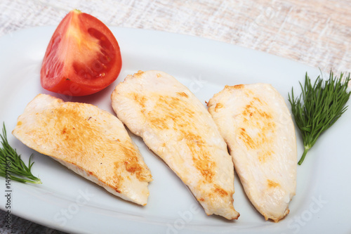 Slices of roasted chicken breast and tomato on white plate