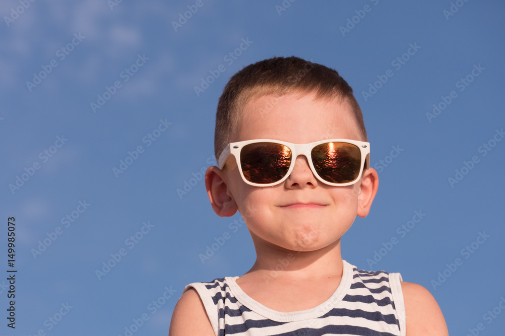 glad little boy wearing sunglasses on blue sky background