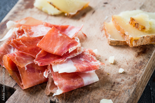 Spanish ham jamon serrano or Italian prosciutto crudo and sliced Italian hard cheese pecorino toscano on old wooden board