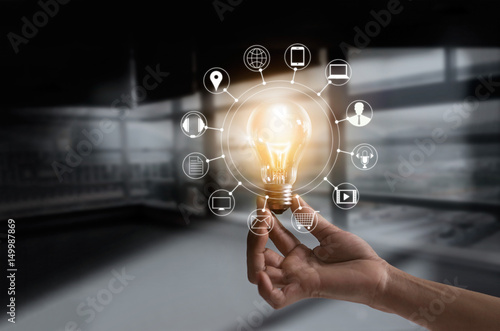 Hand holding light bulb with icons multimedia and customer network connection on dark room background