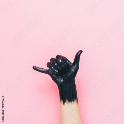 surf Shaka gesture by black painted hand on pink background. minimal style of summer