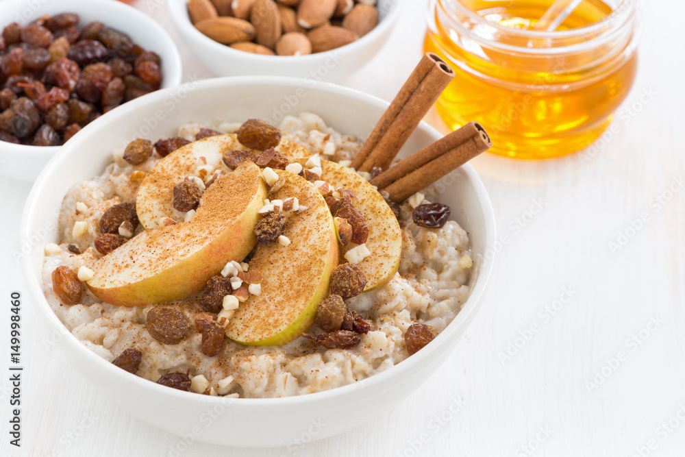 oatmeal with fresh apples, raisins, cinnamon and ingredients on white wooden background, close-up oatmeal with fresh apples, raisins, cinnamon and ingredients on white wooden background, close-up