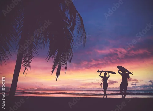 Obraz Sylwetka surfer ludzi niosących deski surfingowe na zachód słońca plaża