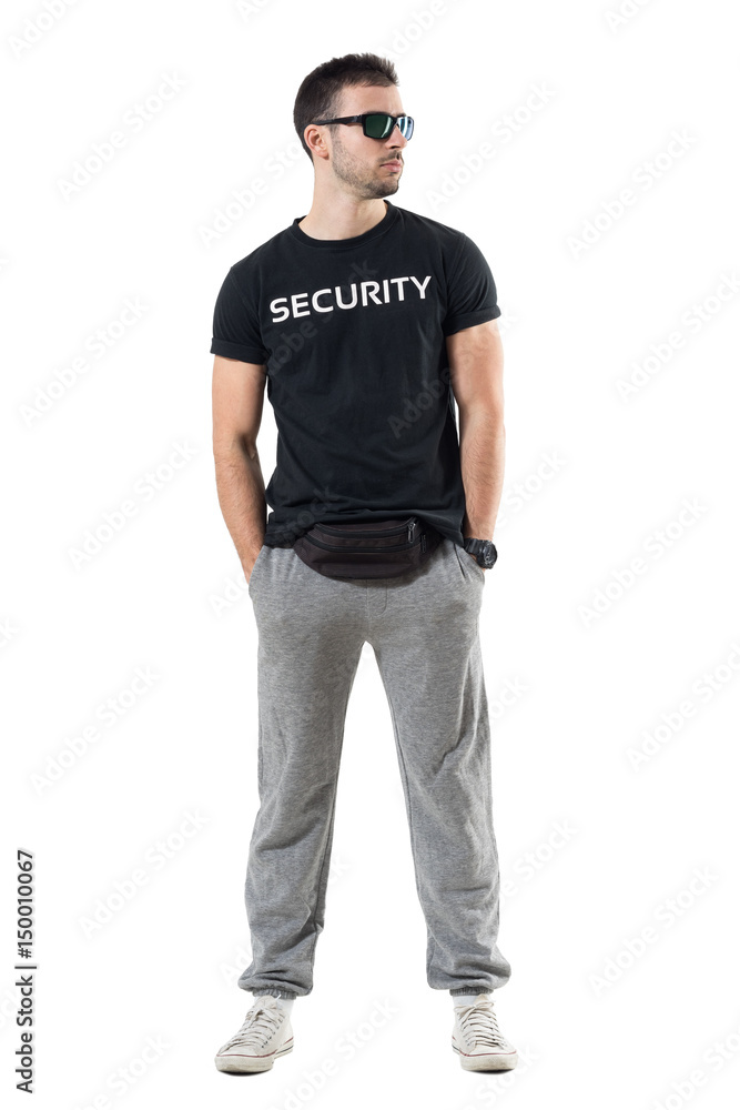 Tough young undercover police agent with waist bag and sunglasses looking away. Full body length portrait isolated on white studio background. Tough young undercover police agent with waist bag and sunglasses looking away. Full body length portrait isolated on white studio background.