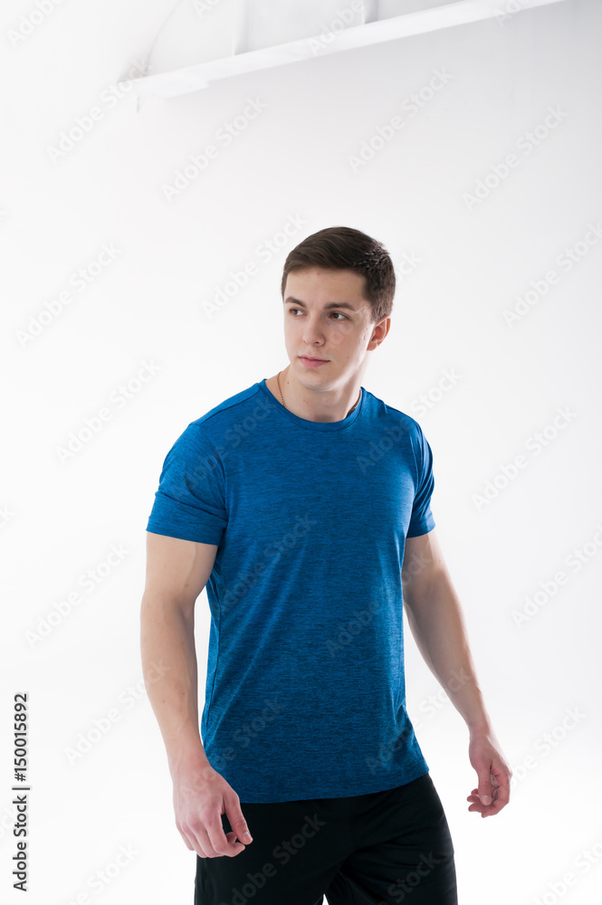 Young muscular handsome athletic man dressed in blue sport shirt, shorts and sneakers standing on white background in studio Young muscular handsome athletic man dressed in blue sport shirt, shorts and sneakers standing on white background in studio