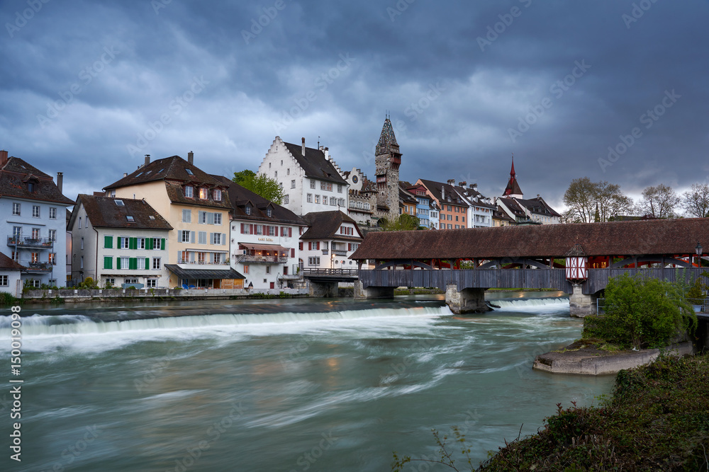 Obraz premium Regenwolken über Bremgarten, Holzbrücke über Fluss Reuss, verwischtes Wasser, Städtchen mit Turm, Kirche und Brücke