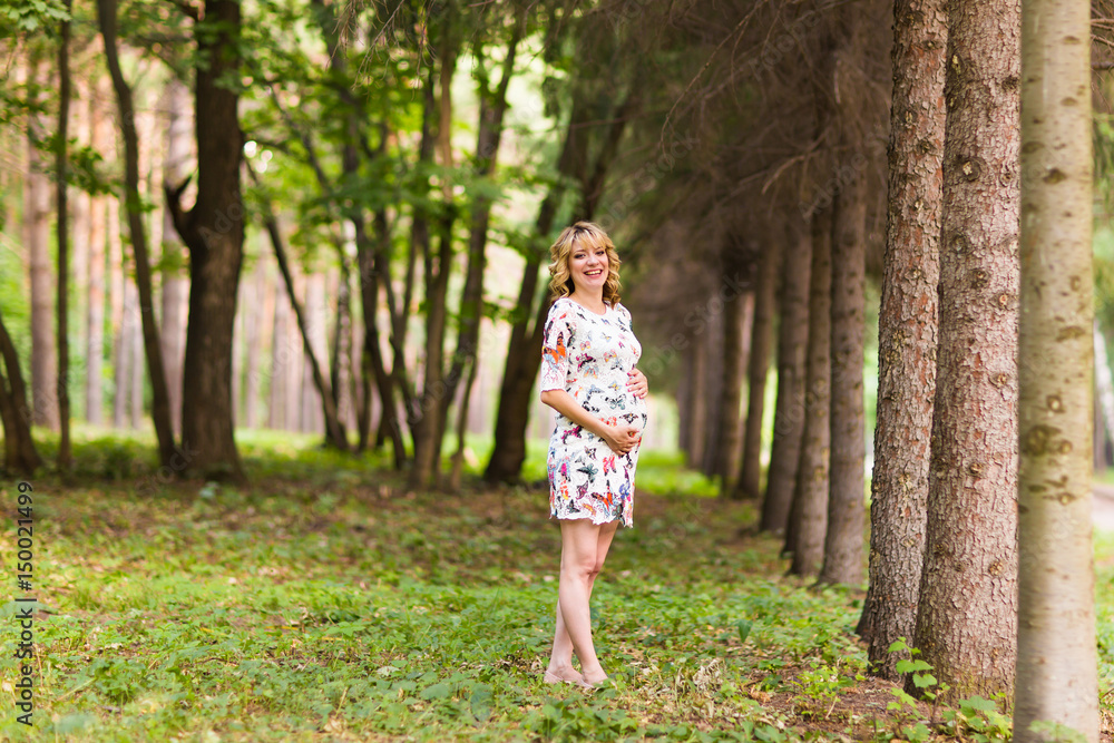 Beautiful pregnant woman touches her belly in the park