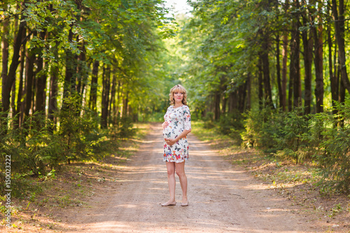 Pregnant woman walking in the park and hugging her pregnant belly. © satura_