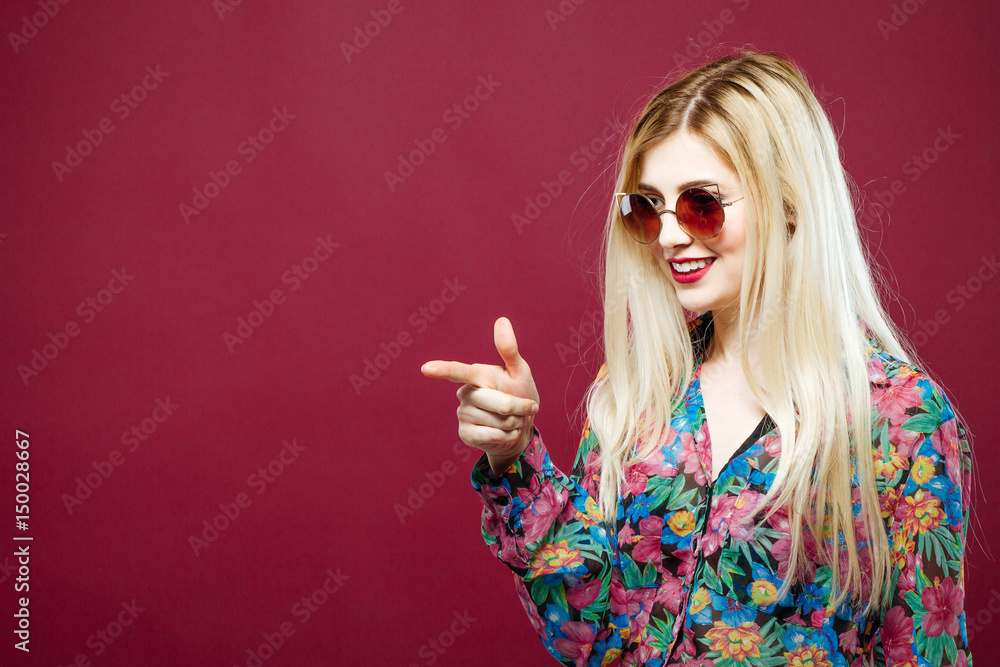 Fototapeta premium Cute Female Model with Sunglasses and Long Hair Wearing Colorful Shirt on Pink Background. Amazing Blonde is Posing in Studio.