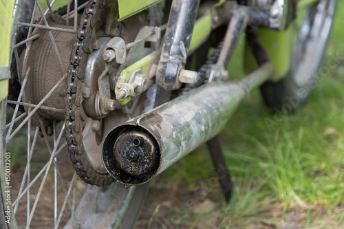 A close-up view of the rear wheel and dirty exhaust of an old motorbike