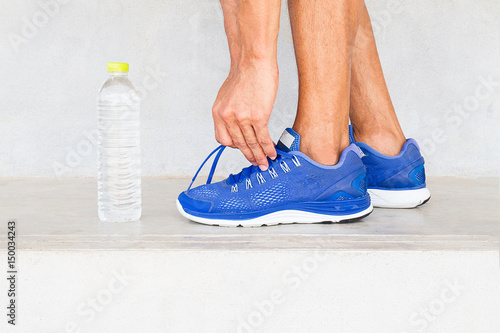 Man lacing sport shoes in gym with water bottle, sport exercise concept