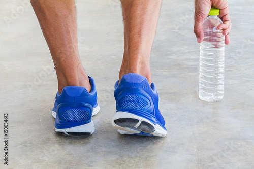 Man wearing sport shoes and picking up water bottle in gym, sport exercise concept