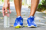 Man wearing sport shoes and picking up water bottle on running track in park, sport exercise concept