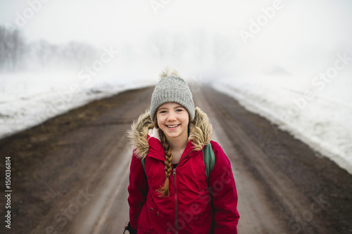 Portrait of girl in knit hat standing in middle of dirt road in fog photo