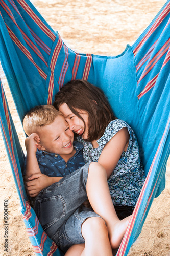 Girl and brother laughing huddled in hammock on Poetto beach, Cagliari, Italy photo