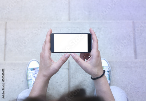 Woman holding modern smartphone. Horizontal mockup. Replaceable with own design. Landscape mode, 16:9 aspect ratio.Top view.