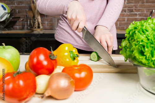 Female cook slicing green cucumber, cooking fresh vegetable salad on cutting board at her kitchen worktop