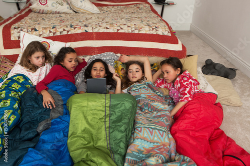 Girls in sleeping bags at slumber party using digital tablet