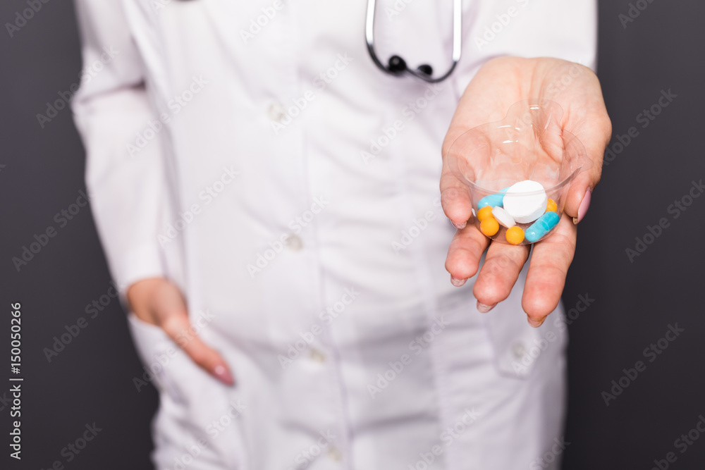 Woman nurse showing pill in hand isolated over grey background.