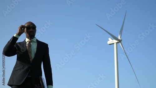 Black man in business suit wearing sunglasses near the background of a wind generator photo